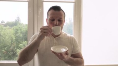Genç ve yakışıklı bir adam pencereden dışarı bakan bir dairedeki fincandan kahve içer. Bir fincandan sade kahve iç. Yavaş çekim