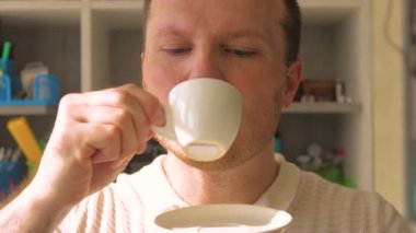 Fincandan sade kahve içen bir adamın portresi. Güzel gülüşü olan genç bir adam kahve fincanından doğal kahve içer. Yavaş çekim