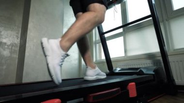 Koşu bandında kardiyo yürüyüşü eğitimi, bir adamın bacaklarına yakın çekim. Spor salonunda elektrikli bisikletle yürümek, ağır çekim..