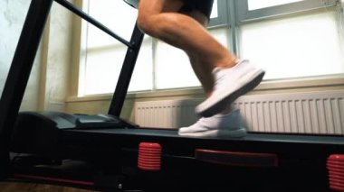 Kardiyo eğitimi, koşu bandında koşmak, beyaz spor ayakkabılı erkek bacakları, yakın çekim, yavaş çekim..