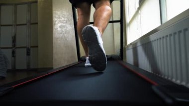 Kardiyo çalışması, koşu bandında yürümek, beyaz spor ayakkabılı erkek bacakları, yakın çekim, yavaş çekim.
