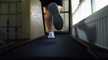 Kardiyo çalışması, koşu bandında koşmak, beyaz spor ayakkabılı erkek bacakları, yakın çekim, yavaş çekim.