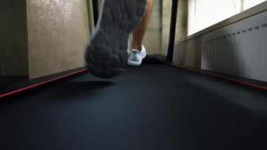 Kardiyo eğitimi, koşu bandında koşan sporcu, beyaz spor ayakkabılı erkek bacakları, yakın çekim, yavaş çekim.