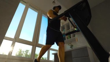 Günbatımı ışınlarının arka planında koşu bandında yürüyen bir kardiyo. Ağır çekim. Simülatörde kardiyo eğitimi.