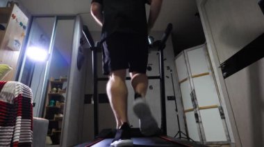 Spor üniformalı bir adam evdeki koşu bandında koşuyor. Kardiyo eğitimi yürüyüşü. Yavaş çekim