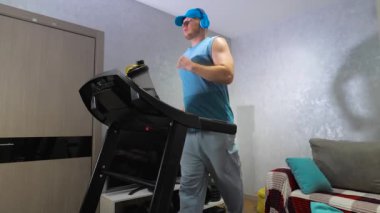 Genç bir atlet iç mekanda kardiyo koşu bandında koşar ve müzik kulaklıklarıyla müzik dinler. Kilo verme konsepti. Yavaş çekim