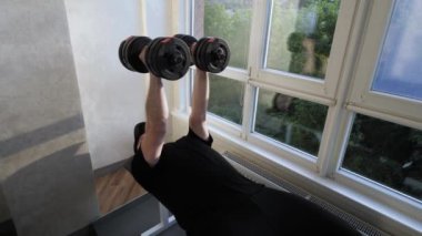 Evdeki spor salonunda aptal göğüs presi. Göğüs kaslarını çalıştıran genç bir adam. Ağır çekim. Ağırlıklarla çalış.