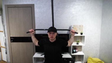 Ağırlık makinesinde evde eğitim, kol pompası. Genç bir sporcu kollarını evdeki bir spor salonunda çalıştırıyor. Yavaş çekim.