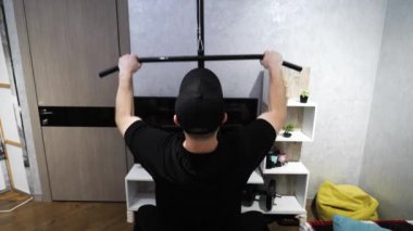 Ağırlık makinesinde evde eğitim, kol pompası. Genç bir sporcu kollarını evdeki bir spor salonunda çalıştırıyor. Yavaş çekim.