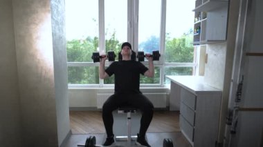 Bir atlet ağırlıkla dambılları kaldırarak omuz egzersizi yapar. Ev antrenmanı. Spor salonunda genç bir sporcu. Yavaş çekim.