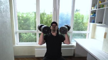 Bir atlet ağırlıkla dambılları kaldırarak omuz egzersizi yapar. Ev antrenmanı. Spor salonunda genç bir sporcu. Yavaş çekim.