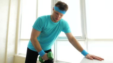 Dambıllarla evde çalış. Bir atlet omuz kasını dambıllarla pompalar. Yavaş çekim