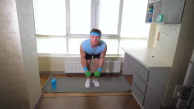 Spor salonundaki halterlerle spor salonu paspası. Genç adam omuzlarını dambıllarla pompalıyor. Yavaş çekim