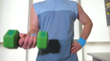 Ellerinde dambıllarla idman yapan genç bir sporcu, antrenman sırasında kolunun pazıları için bir egzersiz yapar.