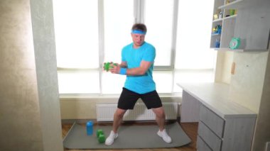 Fitness paspasındaki dambıllarla egzersiz. Evde erkek antrenmanı. Ağır çekim. Spor yaşam tarzı.