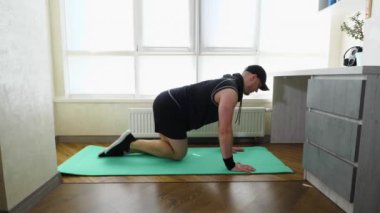 Spor minderinde antrenman yaparken kardiyo egzersizleri, dört ayak üzerinde sallanan bacaklar. Siyah spor üniformalı genç bir adam evde antrenman yapıyor. Yavaş çekim.