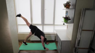  Antrenman evde yapılır. Siyah spor üniformalı genç bir adam spor minderinde bacak sallıyor. Yavaş çekim.