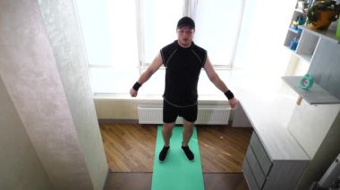 Antrenman sırasında evde bacak sallama. Siyah spor üniformalı bir adam spor yapıyor spor minderinde. Yavaş çekim.
