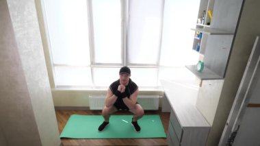 Dizi bükülmüş çömelmiş çömelmeler. Evde idman yapıyorum. Genç bir adam evde spor yapar. Yavaş çekim.