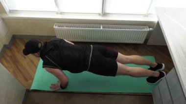 Ev antrenmanı. Zeminden şınav çek, kollarını kaldır. Genç sporcu evde spor minderinde antrenman yapıyor. Yavaş çekim.