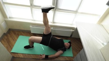 Ev antrenmanı. Sırtınızı ve karın kaslarınızı güçlendirin. Bacaklarını kaldırma egzersizi yap. Genç sporcu evde spor minderinde antrenman yapıyor. Yavaş çekim.
