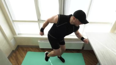 Genç bir adam karın kaslarını şişiriyor, karnını çalıştırmak için bacaklarını kaldırıp evde antrenman yapıyor. Fitness paspası üzerinde egzersiz. Yavaş çekim