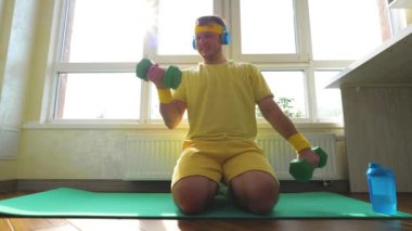 Elinde dambıllarla spor paspasıyla evde antrenman yapıyor, genç bir adam spor egzersizleri yapıyor. Yerde egzersiz yapan çekici, aktif bir adam. Yavaş çekim