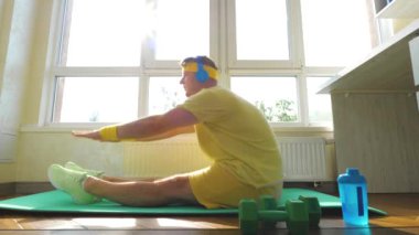 Spor paspasının üstünde vücut kaslarını esneten genç bir adam spor egzersizleri yapıyor. Yerde egzersiz yapan çekici, aktif bir adam. Yavaş çekim