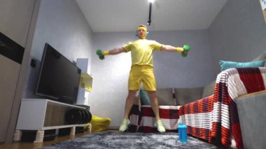 Ellerinde dambıllarla zıplıyorlar. Bir evin içinde antrenman eğitimi aldım. Genç bir adam elinde dambıllarla zıplama hareketleri yapıyor. Yavaş çekim