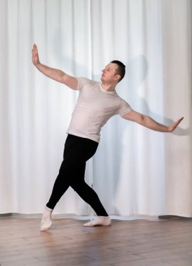 Klasik bale pozu veren bir adam. Ev için dans eğitimi. Genç ve yakışıklı bir dansçı spor pozları veriyor..