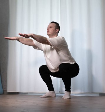Yoga pozisyonunda ev çalışması. Bir adam spor egzersizleri yapıyor, kollarını ve bacaklarını ısıtıyor, erkek bir sporcu esniyor..