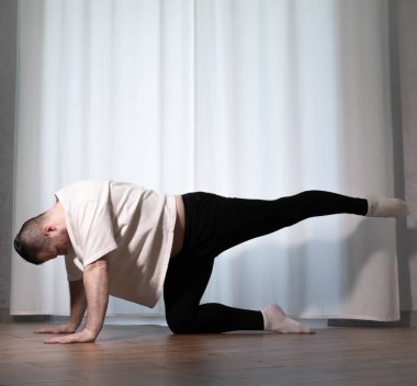 Yoga pozisyonunda ev çalışması. Bir adam spor egzersizleri yapıyor, kollarını ve bacaklarını ısıtıyor, erkek bir sporcu esniyor..