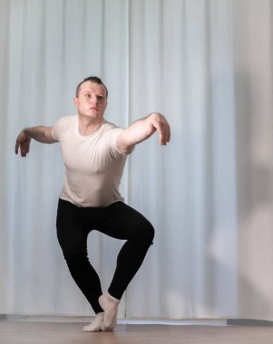 Genç ve yakışıklı bir klasik dansçı dairede ısınıyor. Evde koreografi eğitimi. Vücut germe.