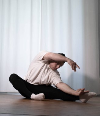 Yoga pozisyonunda ev çalışması. Bir adam spor egzersizleri yapıyor, kollarını ve bacaklarını ısıtıyor, erkek bir sporcu esniyor..