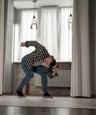 Beyaz arka planda dans eden genç adam. Ekose gömlekle modern dans. Spor plastik hareketler kollar, bacaklar ve gövde.