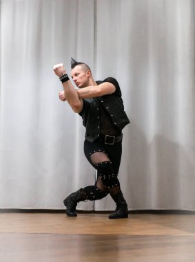 Rock kostümlü bir adam dans figürleri sergiler. Kafasında mohawk olan metal bir adam. Hareket eden adam ve dans eden kollar ve bacaklar..