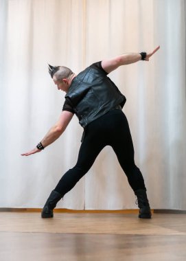 Rock kostümlü bir adam dans figürleri sergiler. Kafasında mohawk olan metal bir adam. Hareket eden adam ve dans eden kollar ve bacaklar..