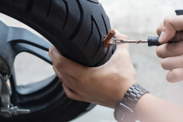 Rider use a tire plug kit and trying to fix a hole in tire sidewall ,Repair a motorcycle flat tire in the garage. motorcycle maintenance and repair concept