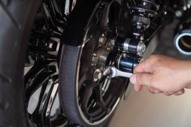 Motosiklet tamircisi bir ingiliz anahtarı kullanır kemer gerilimini ayarlar ve garajda çalışan motosiklet üzerine sürücü kemeri takar. Bakım ve onarım motorsiklet konsepti.