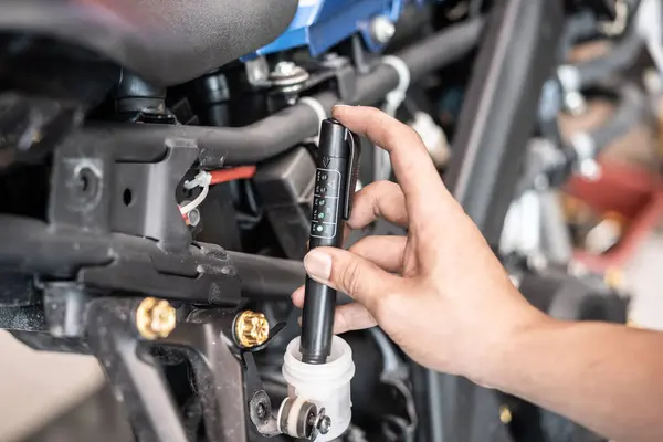 Technician checks brake fluid in motorcycle with Brake Fluid Liquid Tester Quality Check Pen Tool at garage, motorcycle maintenance and repair concept