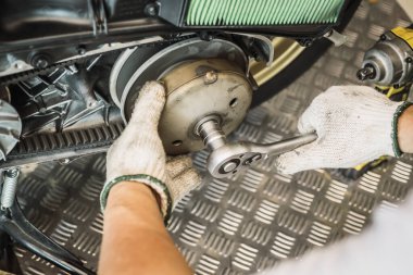 Otomatik iletim sistemini kaldırmak için ingiliz anahtarı ve soketi kullanan tamirci veya scooter motorsikletlerinin arka debriyaj makarasını kullanan, garaj bakımında çalışan, motosiklet konseptini tamir eden, seçici odaklı
