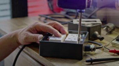 Elektirikli tornavida kullanan bir adam vidayı masadaki lastik blok prizine sokuyor.