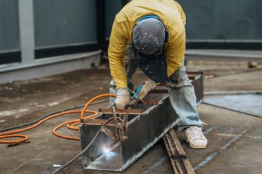 Metal bir plaka kaynakçısı, kaynak başlığı, güvenlik ve çevre konsepti olmadan fabrikanın dışında çalışıyor.