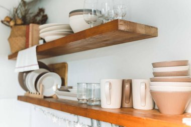 Bardaklı ahşap raf, kahve fincanı, tabak, kase ve çeşitli mutfak süslemeleri. Asılı depo. Organizasyon mutfak odası kavramı 