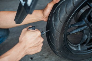 Sürücü lastik tıkaç kiti ya da tıkaç aleti kullanır ve lastiğin yan duvarında bir delik açmaya çalışır, garajda patlak bir motosiklet lastiğini tamir eder. motosiklet bakım ve onarım konsepti  