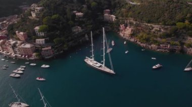 İtalya 'nın Portofino yakınlarındaki bir körfezde İtalyan tarzı evleri olan kayalıklar ve kayalıklarla çevrili büyük bir yelkenli yatının insansız hava aracı görüntüleri.