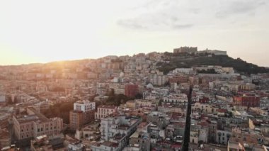 Günbatımında Napoli 'nin çarpıcı hava manzarası, şehrin yoğun kentsel dokusunu tepe binaları ve sıcak altın ışıkla yıkanmış tarihi mimarisiyle gözler önüne seriyor..