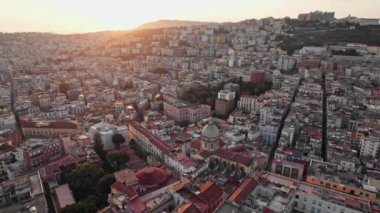 Napoli, İtalya 'nın gün batımında, nefes kesici bir hava manzarası, kalabalık tarihi binaları, dar sokakları ve tepelik bir zemin ve parlayan güneş ışığına karşı kurulmuş kubbeli kiliseleri vurguluyor..