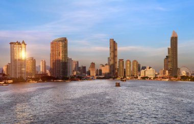 Bangkok şehrinin ön planında nehir manzaralı bir bina. Akşamları ve birkaç bulut var.