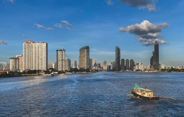 Bangkok şehrinin ön planında nehir manzaralı bir bina. Akşamları ve birkaç bulut var.